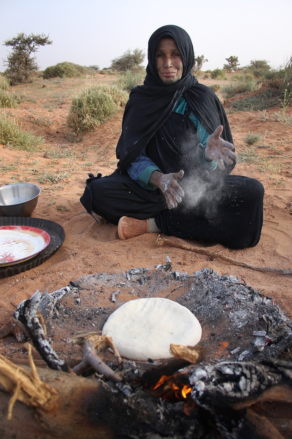 “Saharawi during the daily ritual of preparing the bread; the dough is baked under the desert sand”, fotografiert von Laura Dauden. Lizenz: CC BY-SA 4.0.